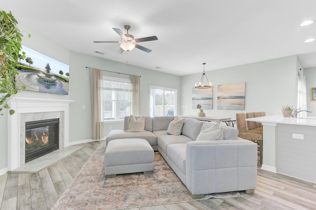 living area with visible vents, a premium fireplace, light wood-style flooring, recessed lighting, and ceiling fan with notable chandelier