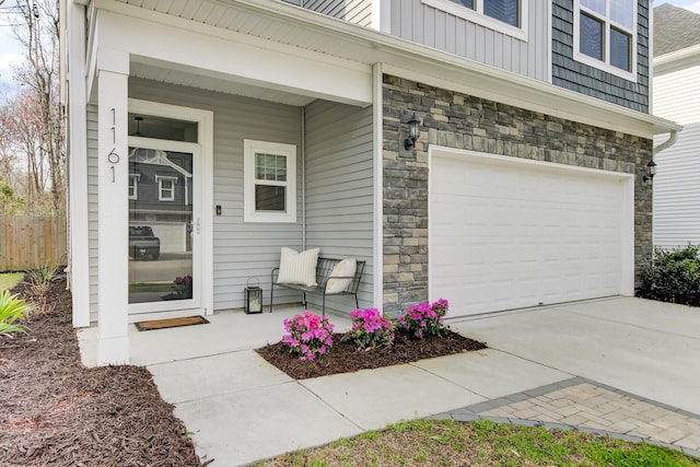 doorway to property with board and batten siding, concrete driveway, covered porch, stone siding, and an attached garage