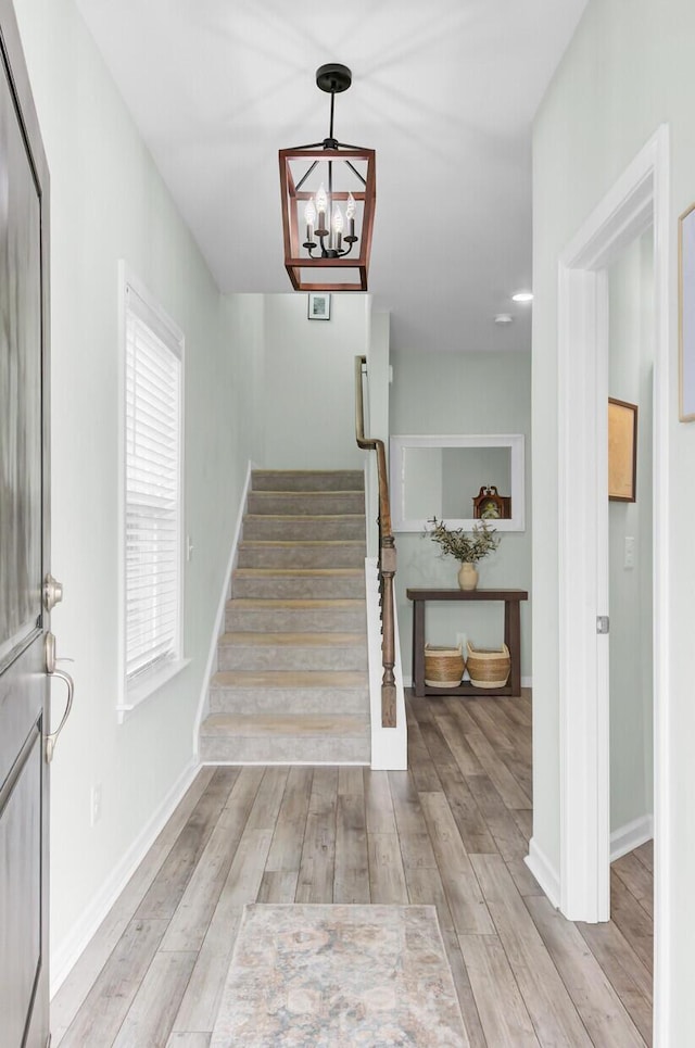 foyer featuring an inviting chandelier, stairway, wood finished floors, and baseboards