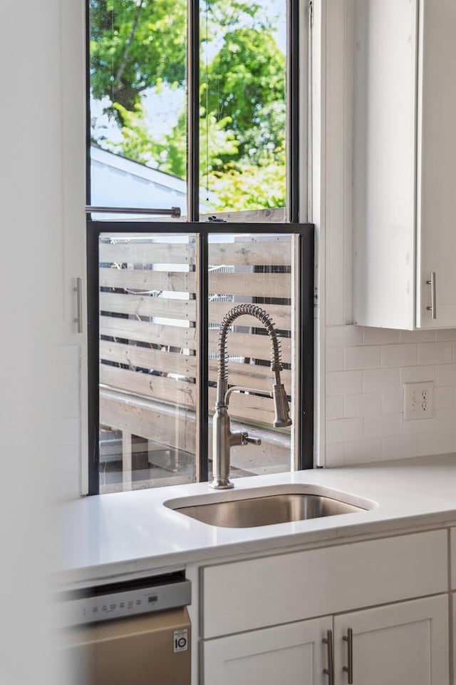 kitchen with decorative backsplash, light countertops, white cabinets, a sink, and dishwasher