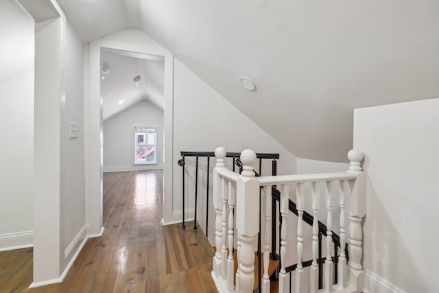 interior space featuring baseboards, hardwood / wood-style floors, vaulted ceiling, and an upstairs landing