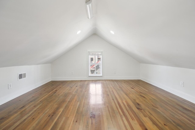 additional living space featuring hardwood / wood-style flooring, visible vents, baseboards, and lofted ceiling