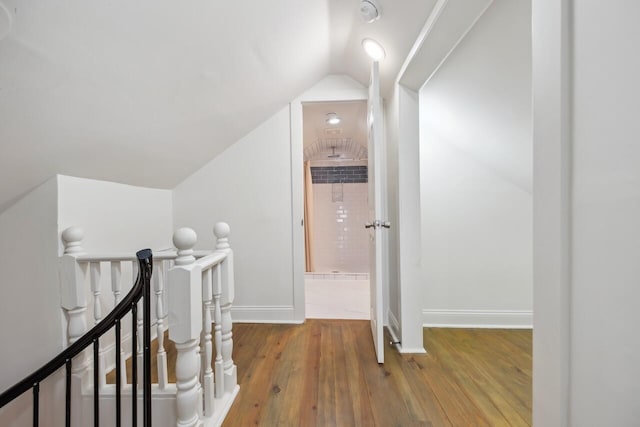 hallway with baseboards, vaulted ceiling, hardwood / wood-style floors, and an upstairs landing