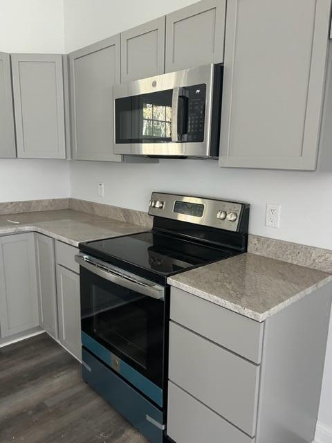 kitchen featuring appliances with stainless steel finishes, gray cabinetry, light stone counters, and dark hardwood / wood-style flooring