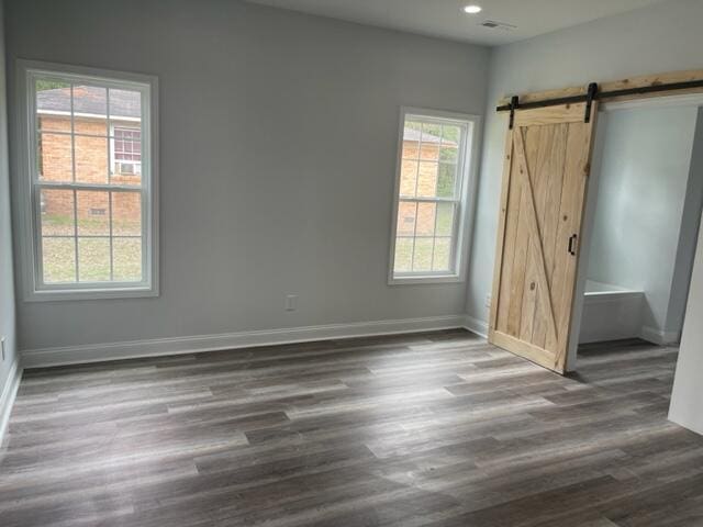 empty room featuring a barn door, dark wood-type flooring, and a wealth of natural light