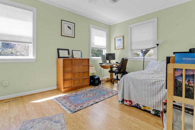 bedroom with visible vents, baseboards, wood finished floors, and crown molding