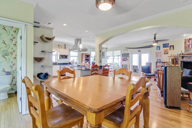 dining room with arched walkways, light wood finished floors, a ceiling fan, and ornamental molding