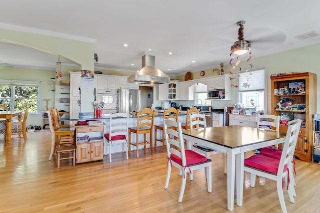 dining room featuring light wood finished floors, visible vents, plenty of natural light, and arched walkways