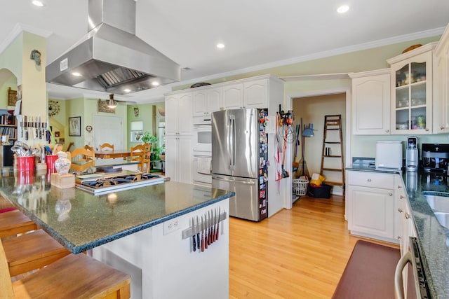 kitchen featuring a kitchen bar, ornamental molding, island exhaust hood, stainless steel appliances, and white cabinetry