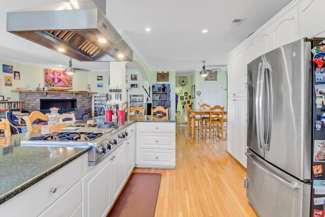 kitchen with light wood finished floors, ceiling fan, range hood, appliances with stainless steel finishes, and white cabinetry