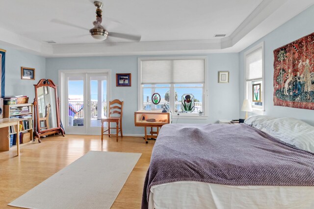 bedroom with a raised ceiling, multiple windows, wood finished floors, and visible vents