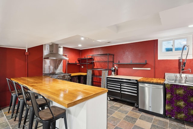 kitchen featuring stainless steel appliances, sink, wooden counters, and wall chimney range hood