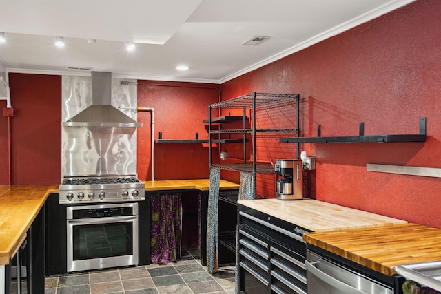 kitchen with crown molding, appliances with stainless steel finishes, wall chimney exhaust hood, and butcher block counters