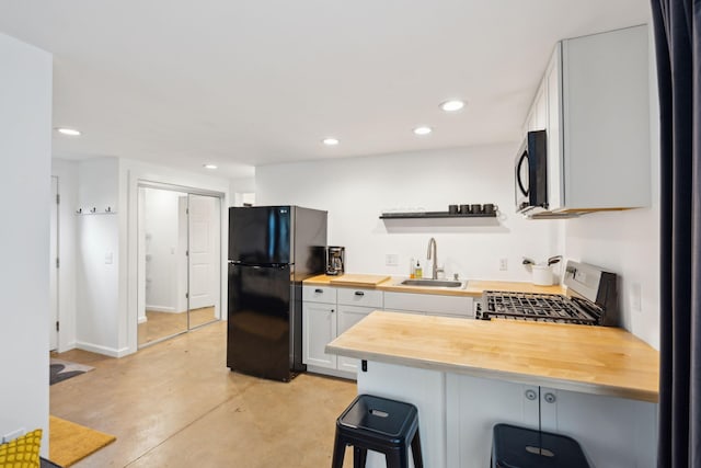 kitchen featuring black fridge, sink, range, and wooden counters