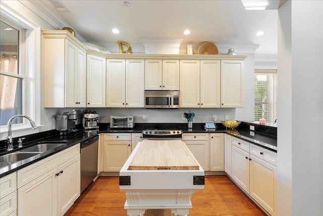 kitchen with sink, appliances with stainless steel finishes, butcher block counters, a center island, and cream cabinets