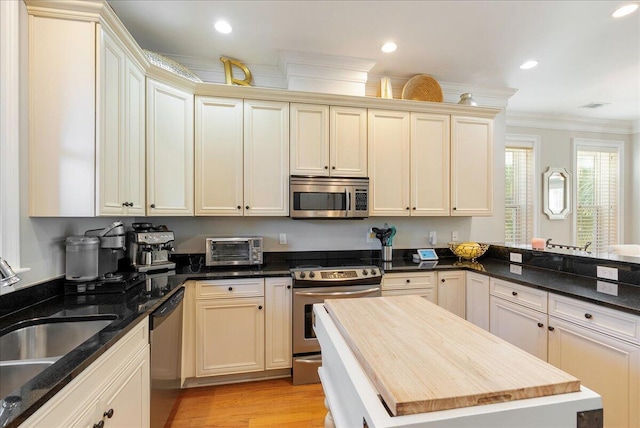 kitchen with cream cabinetry, crown molding, wooden counters, and appliances with stainless steel finishes