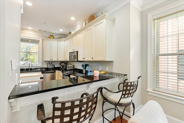 kitchen featuring sink, appliances with stainless steel finishes, a kitchen breakfast bar, ornamental molding, and kitchen peninsula