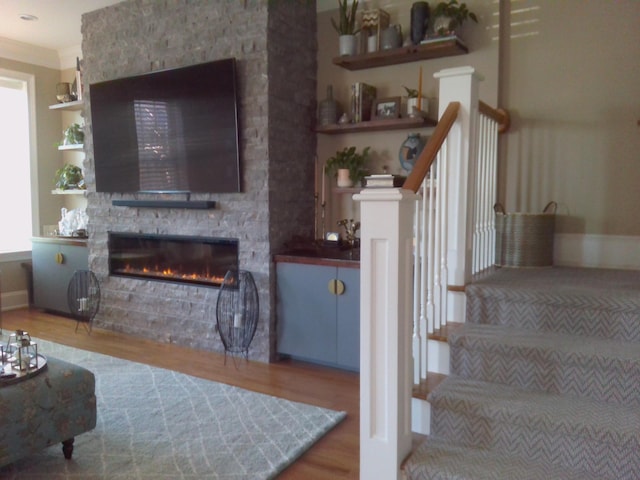 living room featuring hardwood / wood-style flooring, a stone fireplace, and crown molding