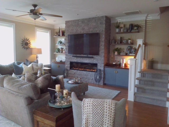 living room with crown molding, wood-type flooring, ceiling fan, and a fireplace