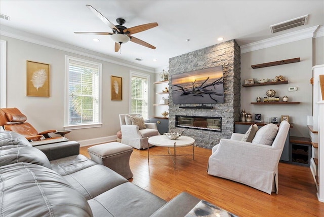 living room featuring crown molding, ceiling fan, wood-type flooring, and a stone fireplace