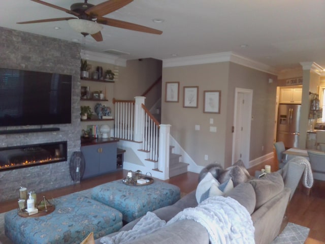 living room with crown molding, wood-type flooring, a large fireplace, and ceiling fan