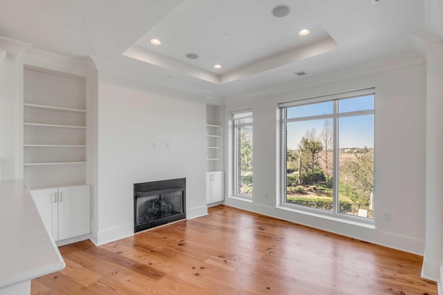 unfurnished living room featuring built in shelves, a fireplace, light wood-type flooring, and a tray ceiling