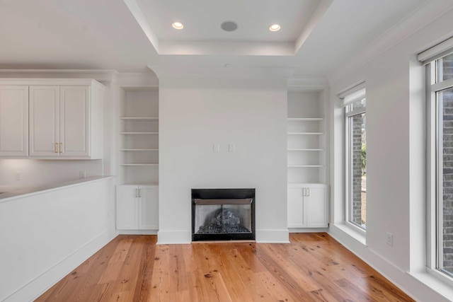 unfurnished living room featuring a raised ceiling, built in shelves, and light wood finished floors