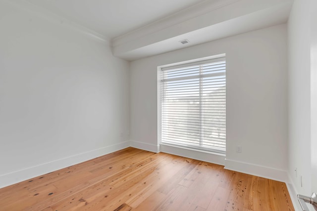 spare room with light wood-type flooring, baseboards, visible vents, and ornamental molding