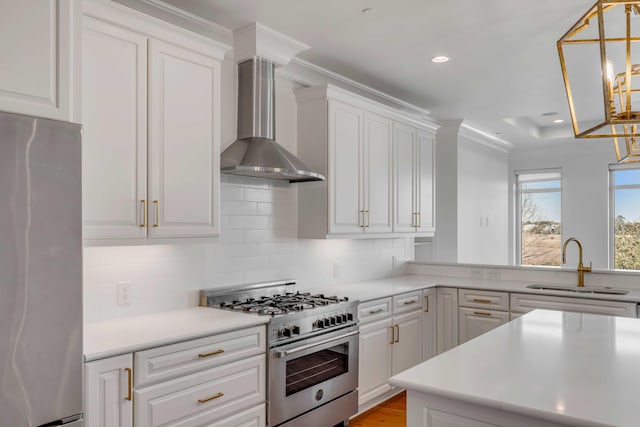 kitchen with a sink, stainless steel appliances, white cabinetry, and wall chimney range hood