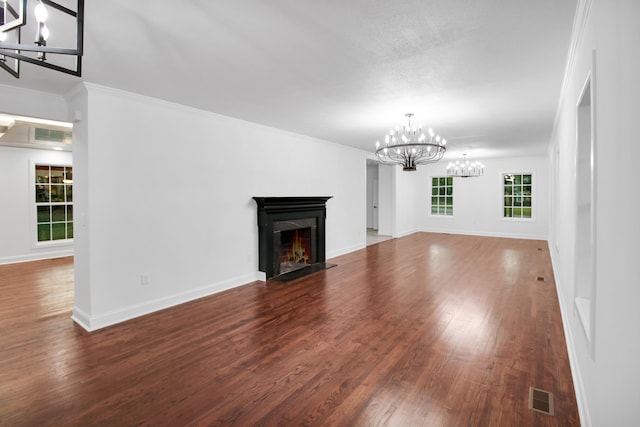 unfurnished living room with wood finished floors, visible vents, baseboards, a lit fireplace, and an inviting chandelier