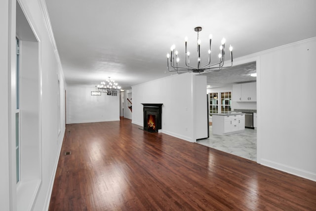 unfurnished living room with a warm lit fireplace, a notable chandelier, baseboards, ornamental molding, and light wood-type flooring