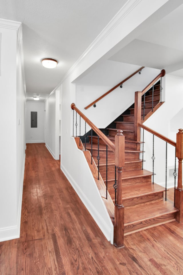 stairway featuring baseboards, electric panel, ornamental molding, and wood finished floors