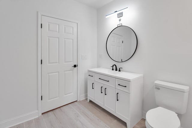 half bath with vanity, wood finished floors, toilet, and baseboards