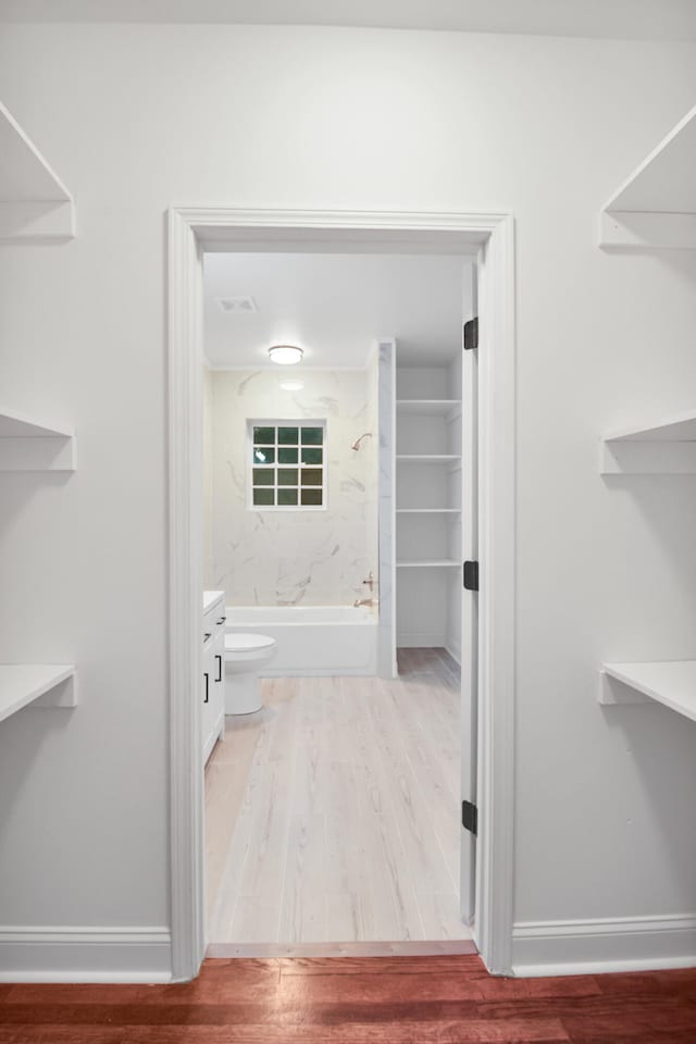 interior space with toilet, wood finished floors, shower / tub combination, and baseboards