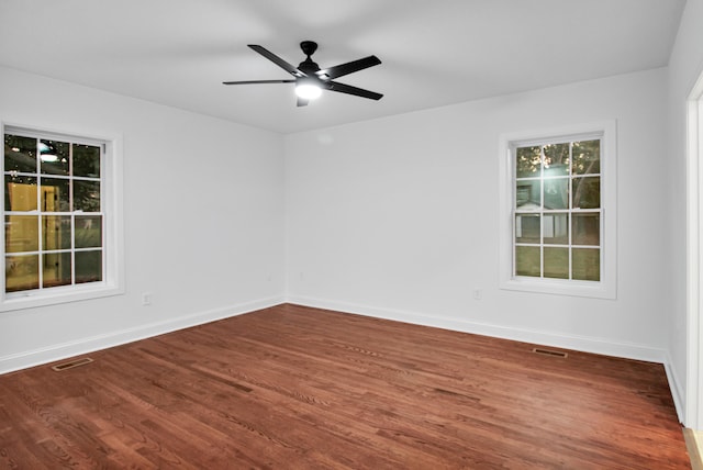 empty room with wood finished floors, visible vents, and baseboards