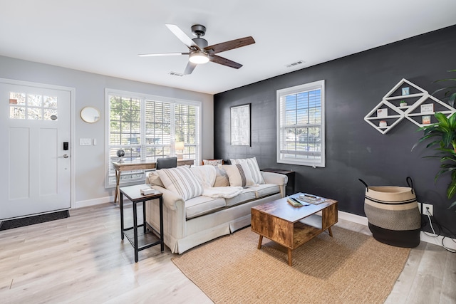 living room with baseboards, light wood-style flooring, visible vents, and a wealth of natural light