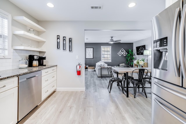 kitchen featuring light stone counters, light wood-style flooring, stainless steel appliances, visible vents, and tasteful backsplash