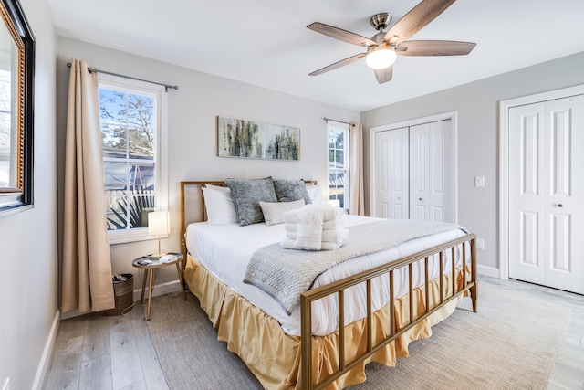 bedroom with light wood-style floors, a ceiling fan, baseboards, and multiple closets