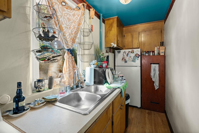 kitchen featuring light countertops, brown cabinetry, freestanding refrigerator, a sink, and wood finished floors