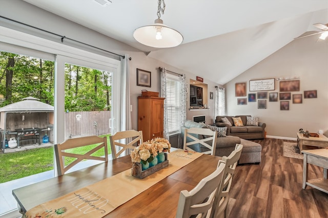 dining room with ceiling fan, a fireplace, baseboards, wood finished floors, and lofted ceiling