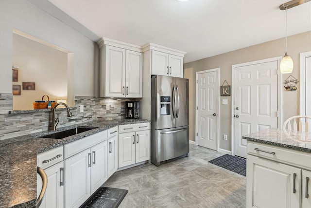 kitchen featuring decorative backsplash, pendant lighting, dark stone counters, stainless steel fridge with ice dispenser, and a sink