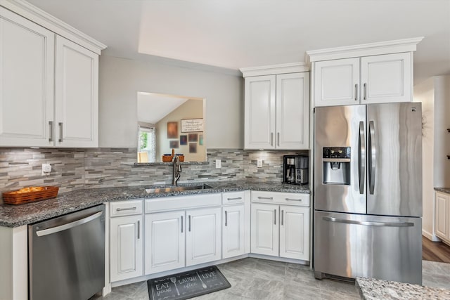 kitchen featuring appliances with stainless steel finishes, a sink, dark stone counters, white cabinetry, and backsplash