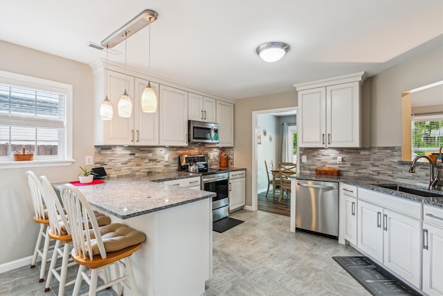 kitchen with a breakfast bar area, backsplash, a sink, a peninsula, and stainless steel appliances