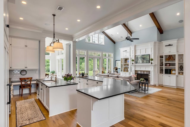 kitchen with white cabinetry, an island with sink, backsplash, a fireplace, and hanging light fixtures