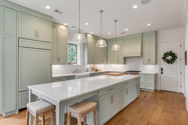 kitchen featuring green cabinetry, pendant lighting, a breakfast bar area, and custom range hood