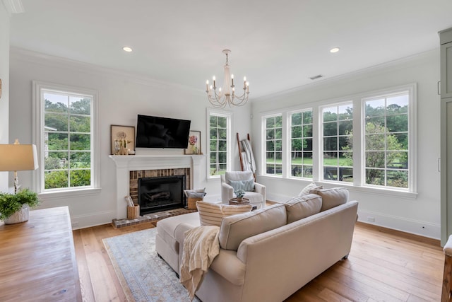 living room with ornamental molding, a fireplace, light hardwood / wood-style flooring, and a notable chandelier