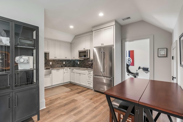 kitchen with appliances with stainless steel finishes, decorative backsplash, light wood-type flooring, lofted ceiling, and white cabinets