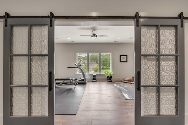 exercise area with ceiling fan, a barn door, and hardwood / wood-style floors