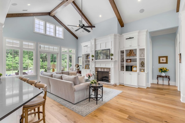 living room with a brick fireplace, ceiling fan, high vaulted ceiling, light hardwood / wood-style flooring, and beam ceiling