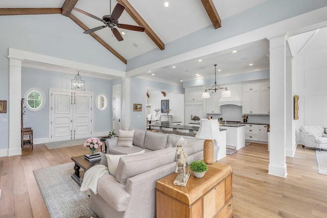 living room with ceiling fan with notable chandelier, ornate columns, beamed ceiling, light wood-type flooring, and high vaulted ceiling